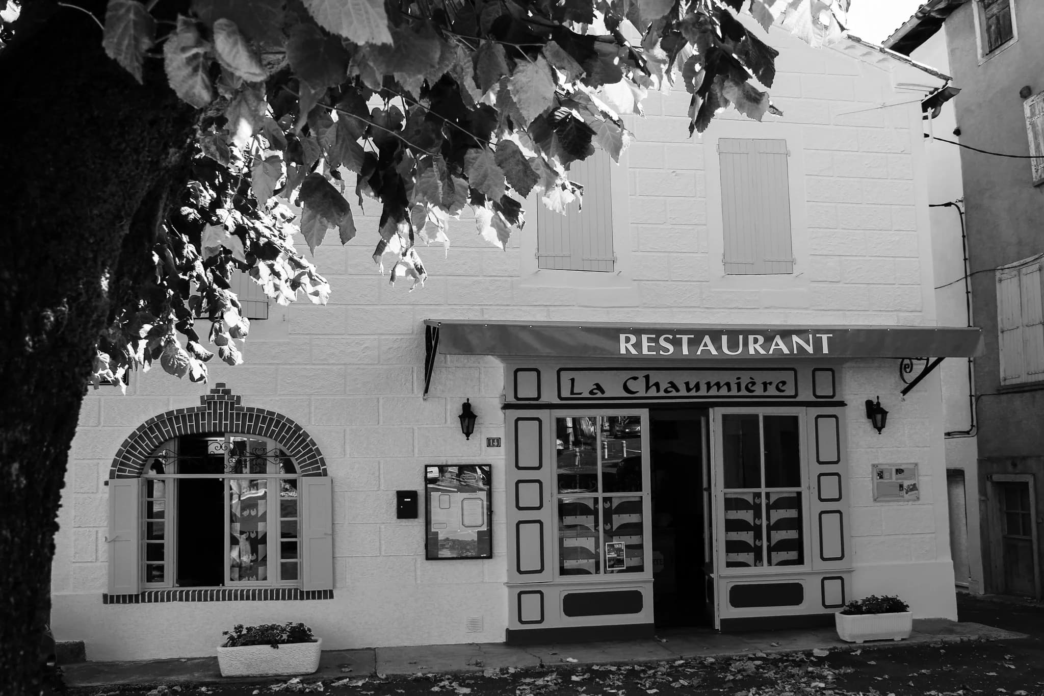 Façade de La Chaumière en noir et blanc sous les arbres